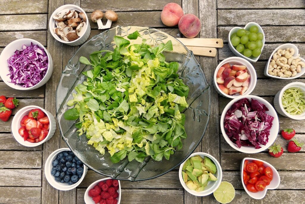 green lettuce leaves chopped in a big ceramic bowl with nuts, fruits, berries on the side