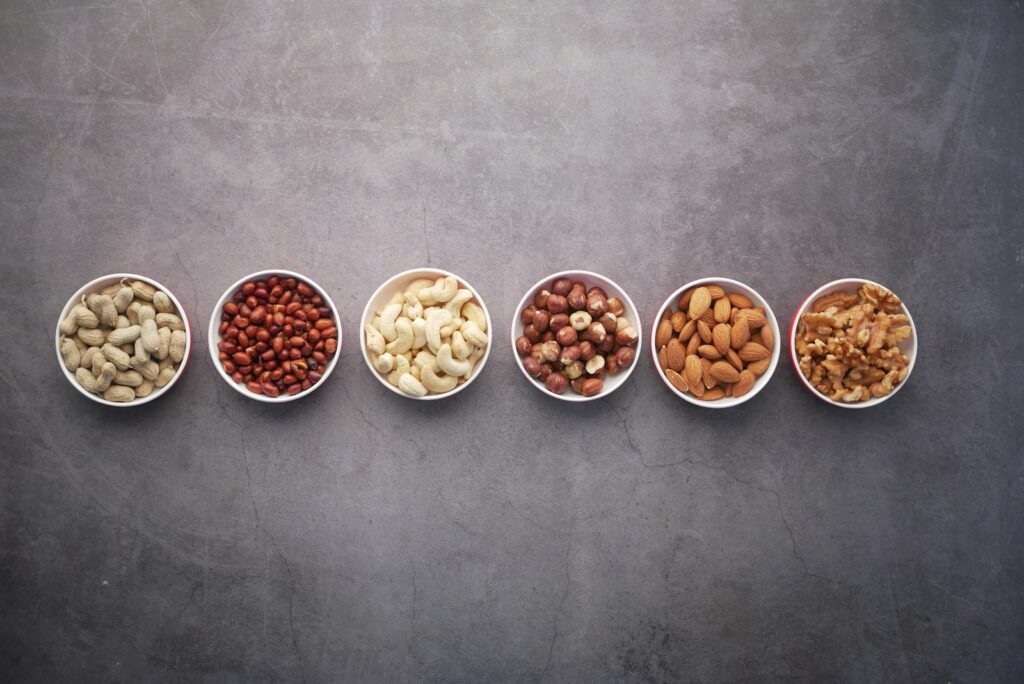 different types of nuts such as peanuts, almond nuts, and legumes placed on white ceramic bowls