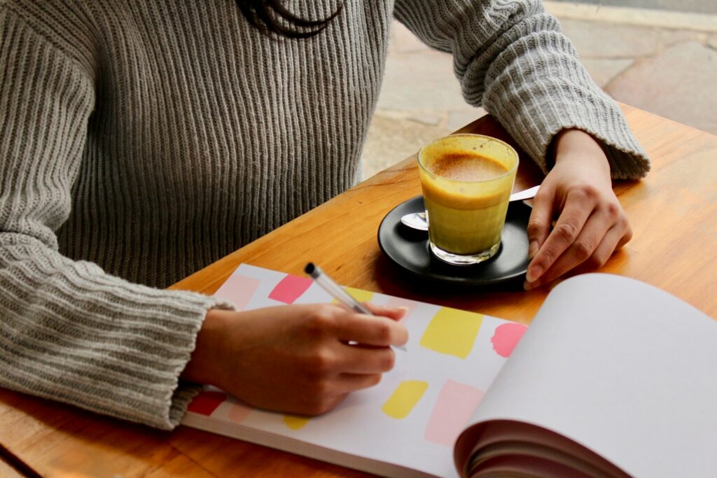 a university student writing notes while sipping a cup of cappuccino coffee on wood table