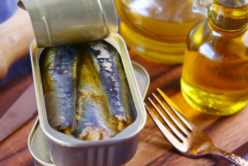 an opened tin can of sardines submerged in extra virgin olive oil sitting on top of a wooden table