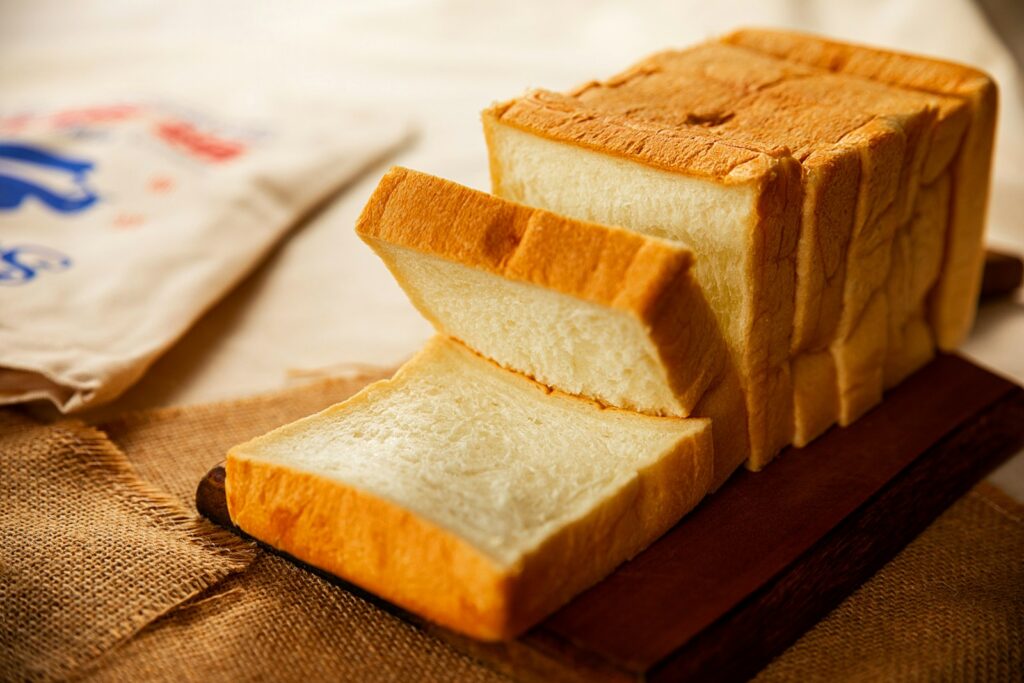 white loaf bread made of all purpose flour sliced thickly on brown wooden tray