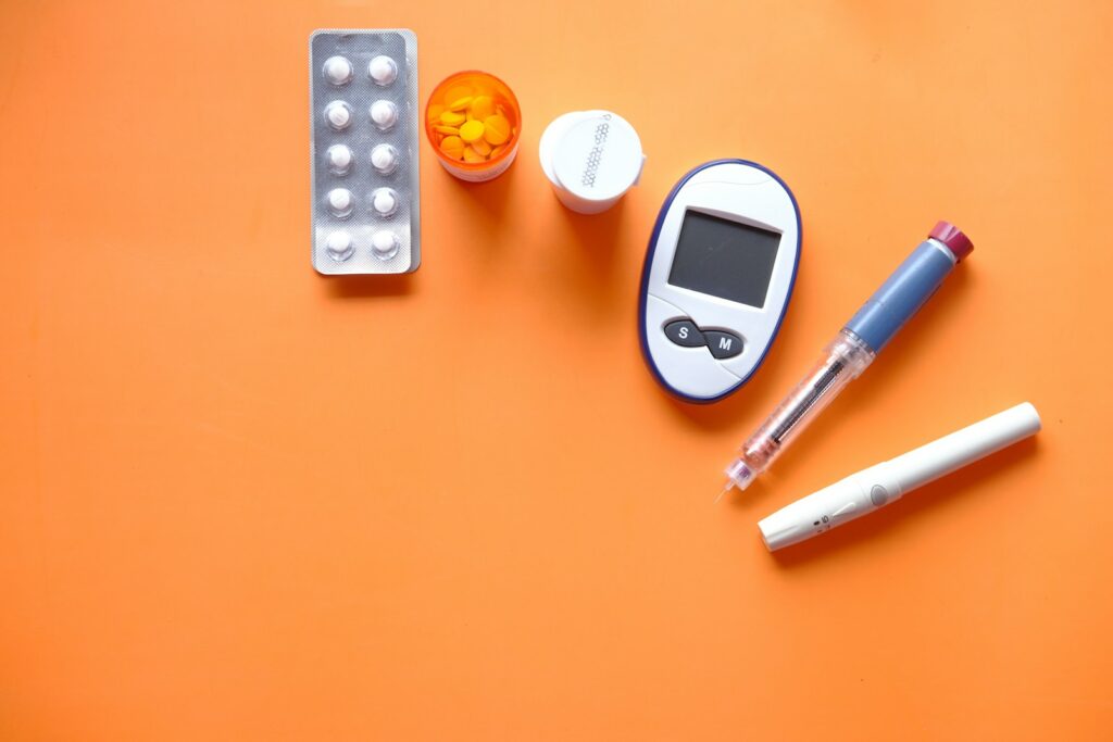 bunch of diabetes treatments place on top of an orange surface such as blood sugar level monitor, insulin injections, and pills for diabetes
