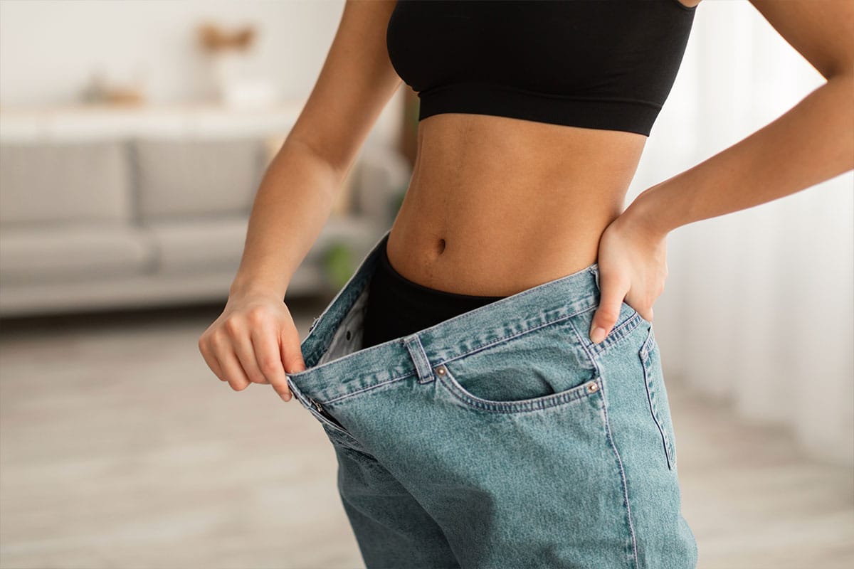 woman in baggy pants showing weight loss results from taking Genesis Supplements